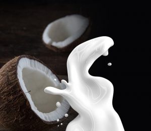 An image of a coconut with milk pouring out of it to discuss consuming less sugar with plant-based milks.