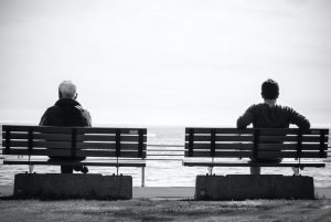 An old man sitting on a bench and a younger man sitting on a bench next to him representing how we shouldn't wait till old age to deal with our pain.
