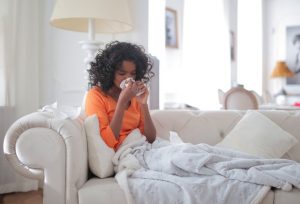 An image of a girl on a couch blowing her nose to talk about how I overcame my allergies and how it relates to my immune health.