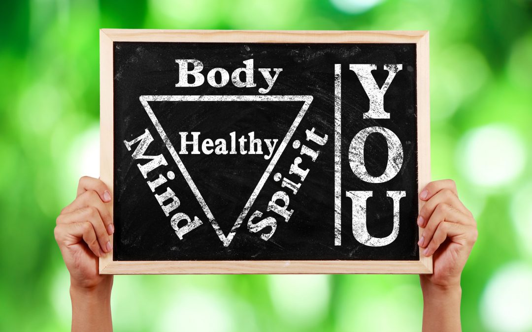 Hands holding blackboard with text You Body Spirit Soul Mind Healthy against green blurred background to represent how in order to be healthy you need to consider "body mind spirit" and understand they are all connected..