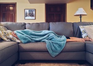 An image of a girl sick on the couch to discuss how environmental factors can be the cause of a person's illness. 