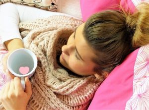 An image of a girl laying down drinking tea trying to rest and fix her immune system this image represents how to notice your immune system is weak and then properly take care of it.