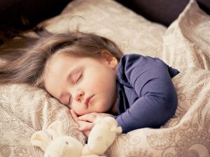 An image of a little girl sleeping with a stuffed rabbit to discuss how much sleep is needed based on age.