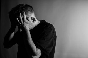 An image of a man in black clutching his head in pain to talk about how sleep deprivation can cause many chronic health conditions.