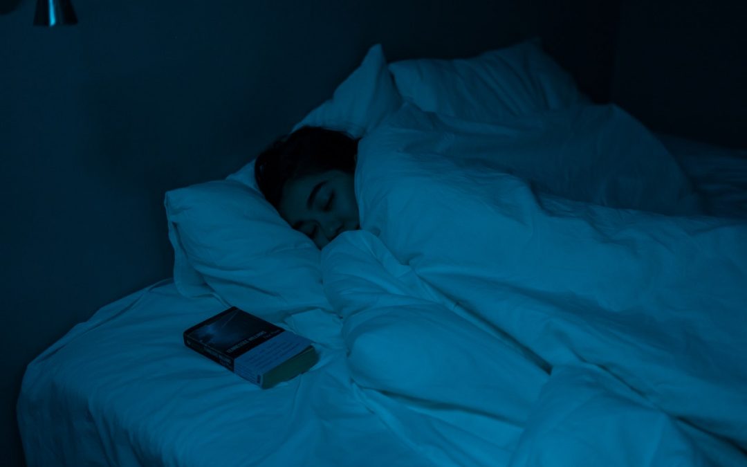 An image of a girl sound asleep in a dark room to discuss how to be a deeper sleeper and get more sleep.
