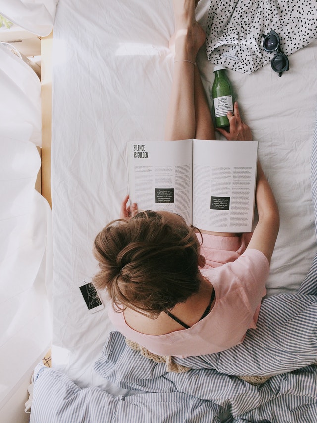 An image of a woman reading in bed to discuss activities to do before bed that can help with sleep.
