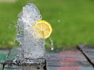 An image of water overflowing with a lemon in it to talk about why drinking enough water is essential for your health