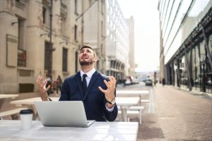 An image of a man staring at the sky with his hands up in frustration and stress.