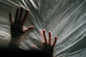 An image of two hands trapped behind a plastic curtain to talk about how stress can make you feel trapped.