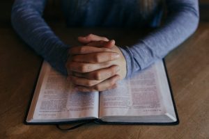 An image of a person's hands praying over their bible to talk about how this is an effective way of managing stress.