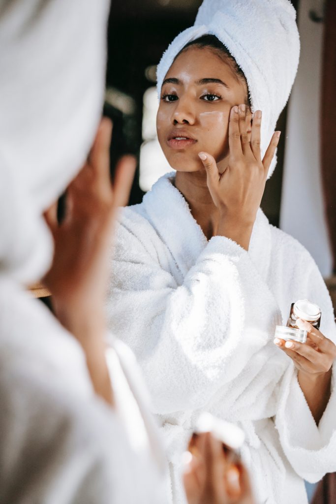 An image of a woman in a white bath robe applying lotion to her face to talk about how most skin care products often contain toxic ingredients.