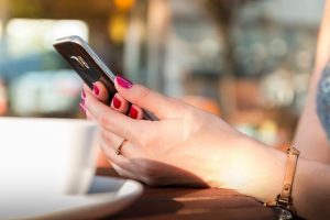 An image of a person on their phone at a coffee shop to talk about ways to spend less time on your phone.