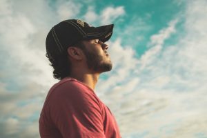 An image of a male with clouds behind him who is feeling more at peace. This is one of the many benefits of meditation.