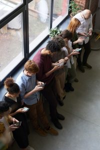 An image of a line of people all staring at their phones to talk about how we are losing the ability to make genuine connections.