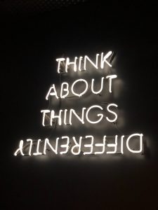 The words "think about things differently" lit up against a black background to talk about how we need to open our minds to thinking differently in order to be present in a community. 