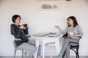 An image of two people drinking coffee and chatting to talk about how to communicate well with anyone. 