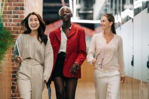 Three woman walking confidently down a work hallway to talk about the benefits of faking confidence until you feel confident.
