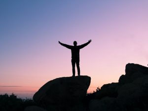 An image of a guy standing on a rock with his arms in the air to show he is feeling secure in himself. 