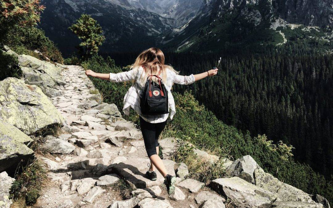 A woman happily hiking through the mountains to talk about finding happiness on a deeper level.