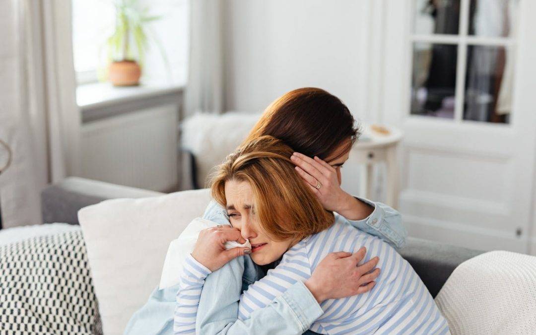 An image of two people hugging to comfort one person who is crying to talk about fully feeling all your emotions.